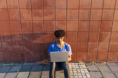 Young man using laptop for studying sitting leaning on wall