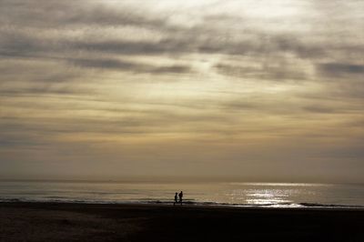 Silhouette man standing on beach against sky during sunset