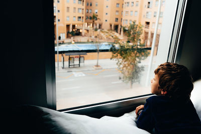 Rear view of boy looking through window