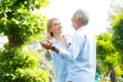 Senior man and mature woman dancing against trees