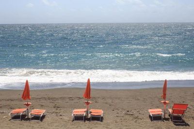 Deck chairs on beach against sky