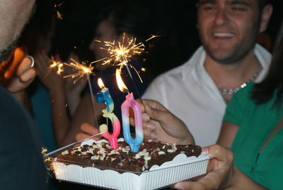 Midsection of woman holding birthday cake with friends at night