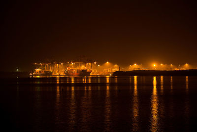 Illuminated city by sea against sky at night