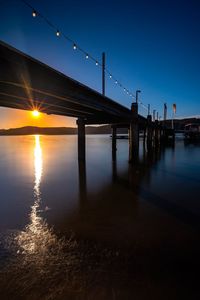 Silhouette bridge over sea against sky during sunset