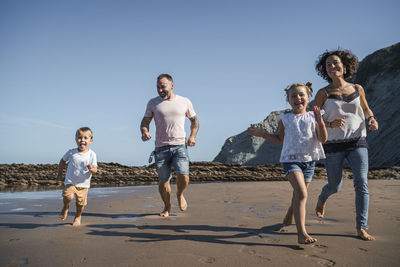 Family having fun while running on beach against sky