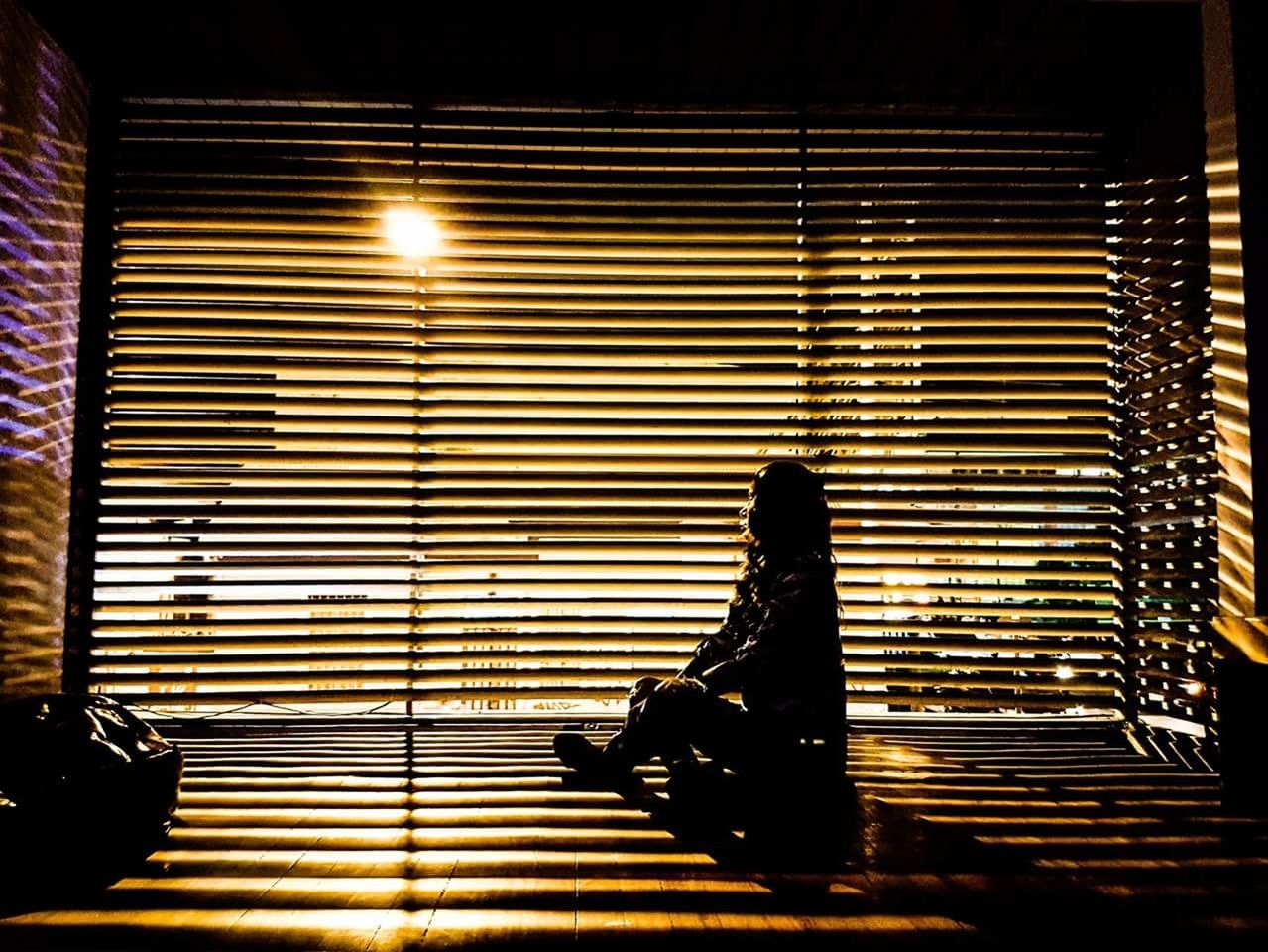 WOMAN SITTING BY WINDOW WITH ILLUMINATED LIGHTS