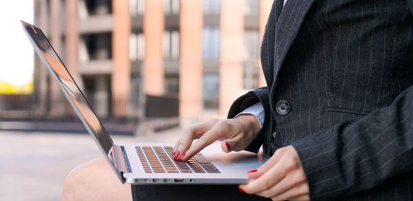 Young serious business woman with laptop studying online while sitting on bench