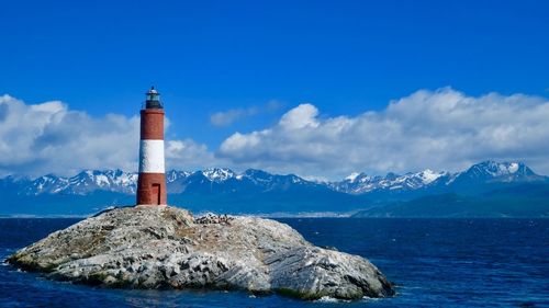 Lighthouse by sea against blue sky