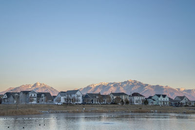 Houses by lake against clear sky during sunset