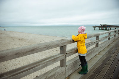 Side view of girl standing on pier looking at sea against sky