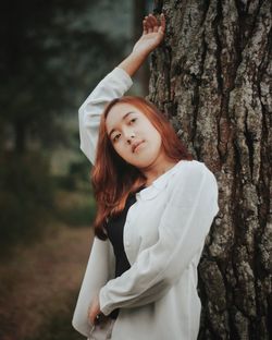 Portrait of beautiful woman standing by tree trunk