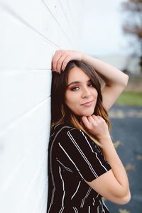 Side view portrait of young woman standing by white wall