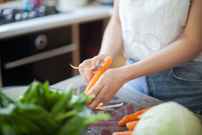 Midsection of woman peeling carrot in kitchen