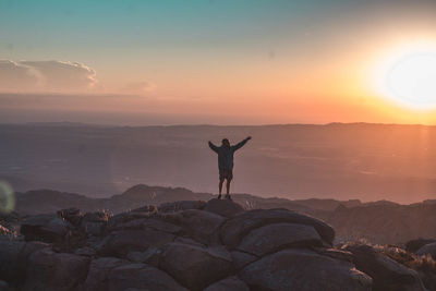 Man standing on rock against sky during sunset