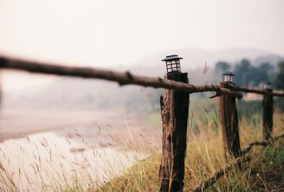 Wooden post on field by fence against sky