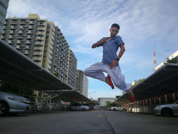 Boy jumping on road in city against sky