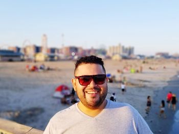 Portrait of smiling man wearing sunglasses at beach against sky