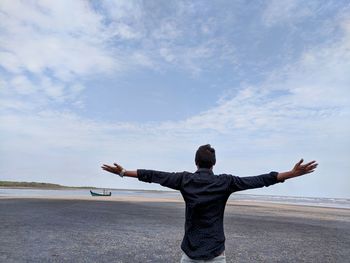 Rear view of man with arms outstretched standing against sky