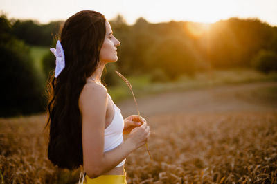 A girl runs through a field with spikelets against the background of the setting sun