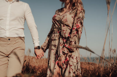 Woman in a print dress and  man in a white shirt holding hands in the middle of wheat field 