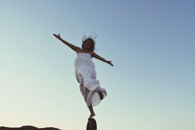 Low angle view of woman with arms outstretched against clear sky