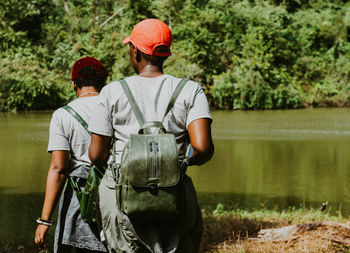 Rear view of women standing by lake against trees