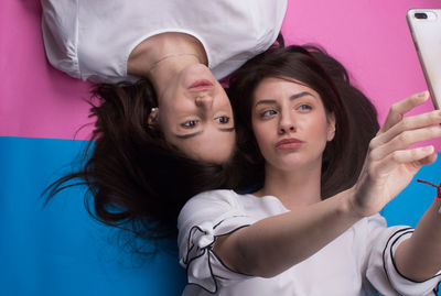 High angle view of female friends taking selfie while lying on colored background