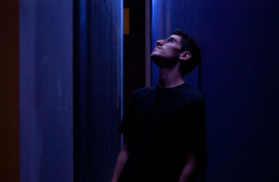 Thoughtful young man looking up while standing by wall at night