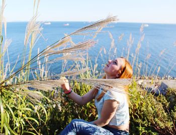 Young woman sitting by plants against sky