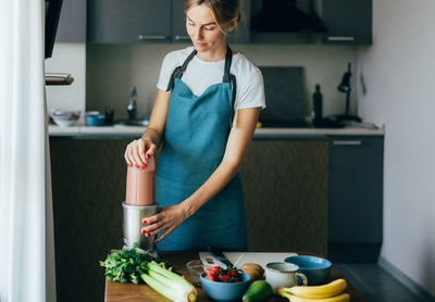 Woman preparing smoothie in kitchen