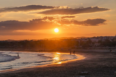 Silhouette people on beach against sky during sunset