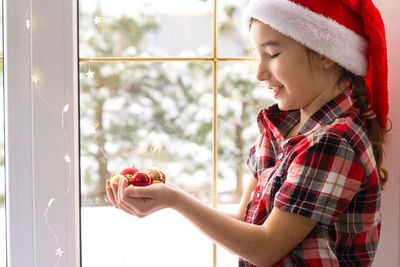 Side view of girl blowing bubbles while standing by window