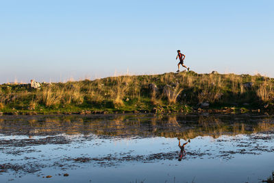 Man jumping over lake against sky