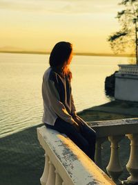 Woman looking at sea against sky during sunset