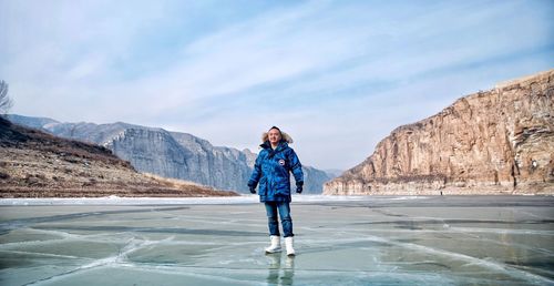 Full length of young woman standing on rock against sky