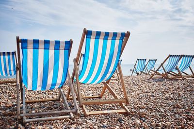 Empty chairs at beach against cloudy sky