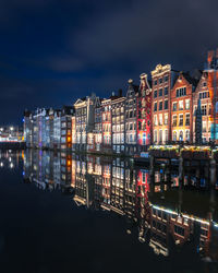 Illuminated buildings by river against sky at night