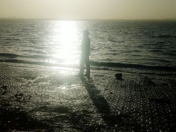 Silhouette woman standing on beach against sky during sunset