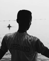 Rear view of man standing at beach against sky