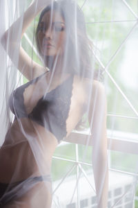 Seductive woman wearing lingerie while standing behind window curtain