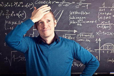 Frustrated teacher standing against blackboard in classroom