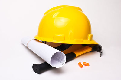 Close-up of hardhat with blueprint and hammer against white background