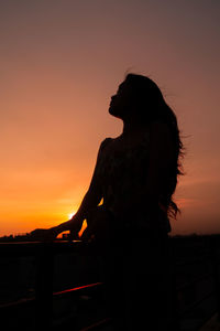 Silhouette woman standing against orange sky during sunset