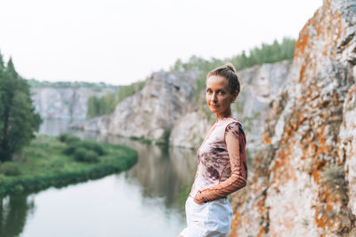 Young slim woman looks at the beautiful view of the mountains and calm river, local travel