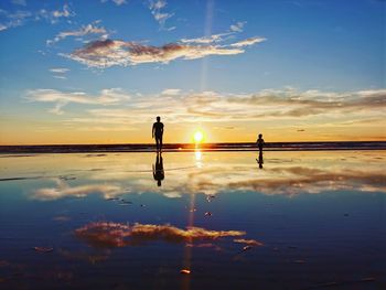 Silhouette people standing on shore against sky during sunset