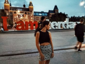 Woman looking over shoulder while standing on street in city