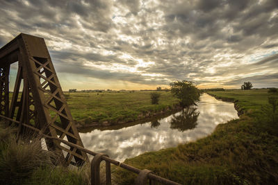 Scenic view of river throughfield against cloudy sky