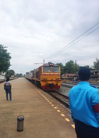 Rear view of man standing on train against sky