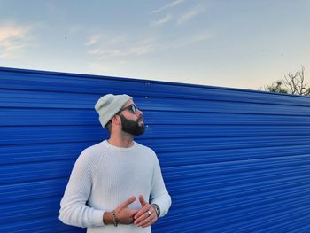 Man looking away while standing against blue retaining wall