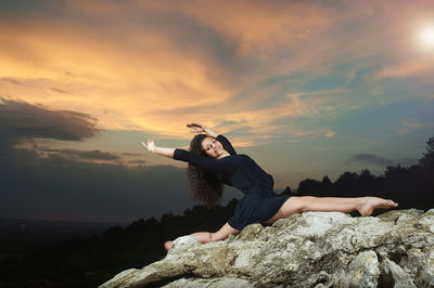 Woman standing on rock against sky during sunset